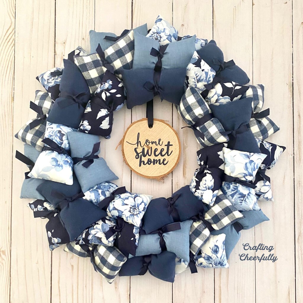 Handmade pillow wreath in blue and white fabrics with a wood slice hanging in the center that says "Home Sweet Home"