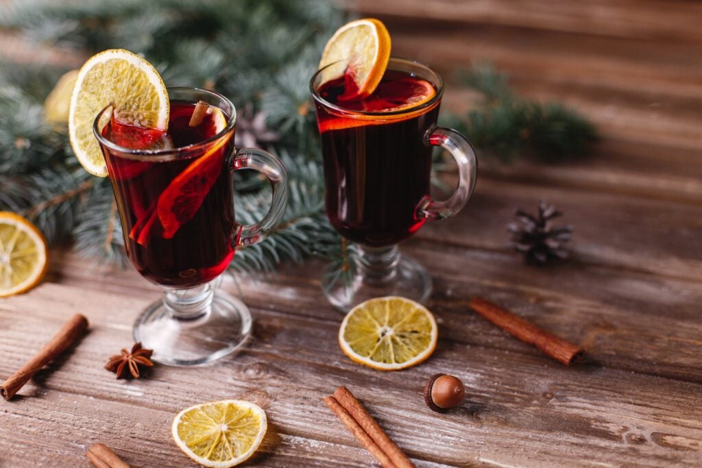 Christmas and New Year decor. Two cups of mulled wine with oranges stand on a wooden table covered with green tree branches