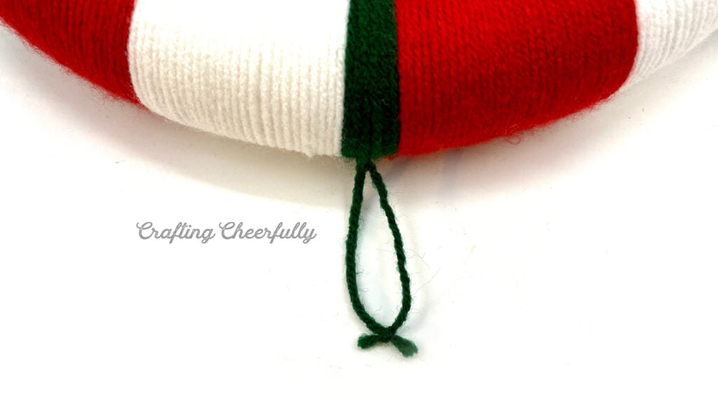 A green yarn hanging loop is added to the top of the wreath.