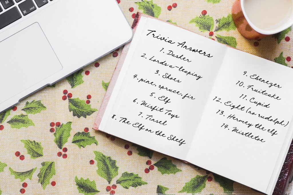 A notepad open to trivia answers lays on a holiday tablecloth by a laptop.
