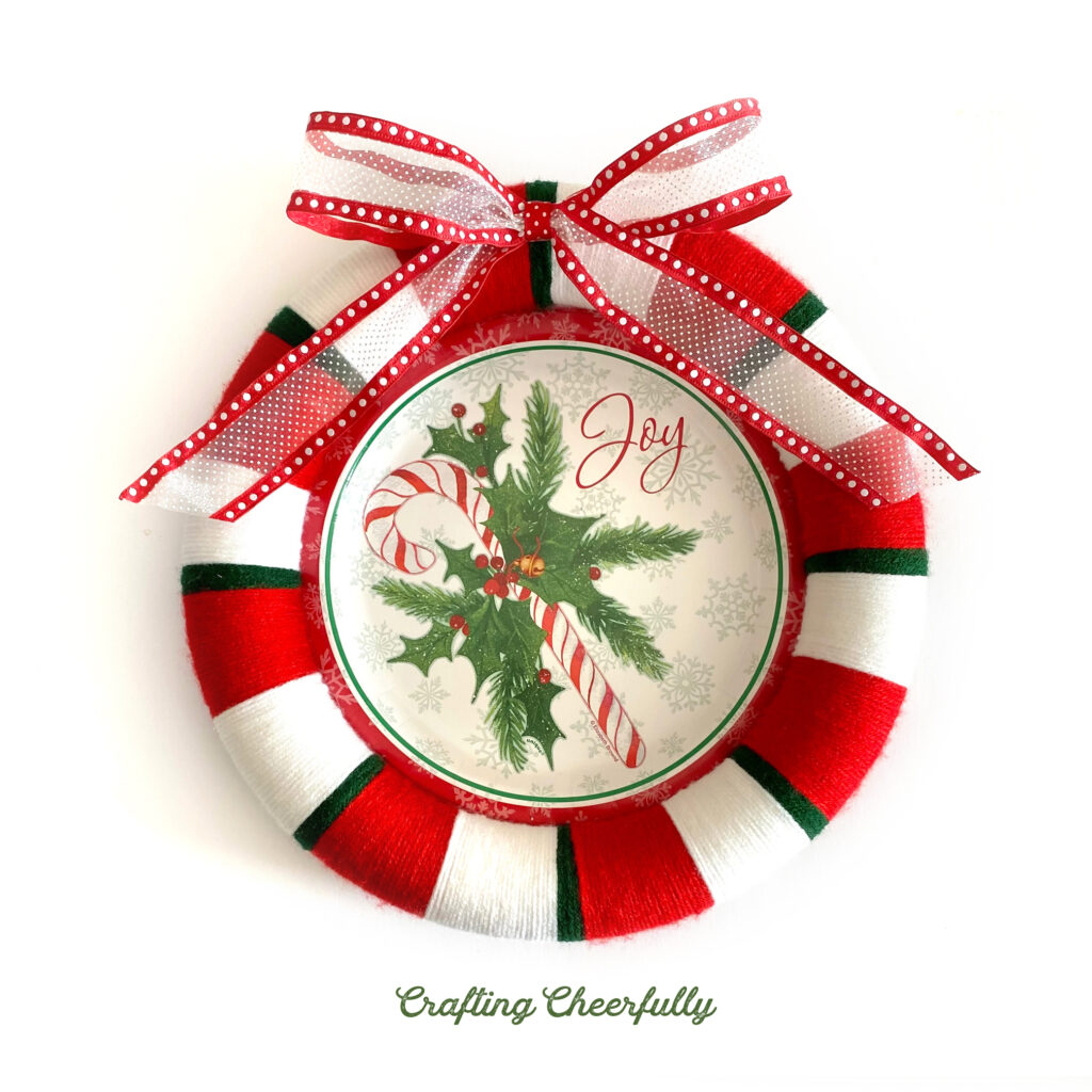 A holiday wreath made from a holiday paper plate and red, white and green yarn with a white and red bow at the top!