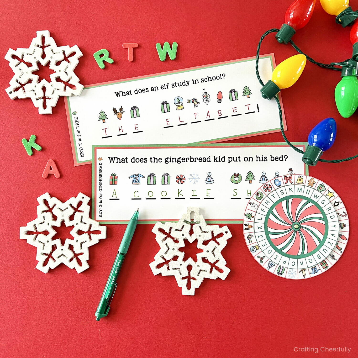 Printable Christmas riddles and decoder wheel lay next to a snowflakes and lights.