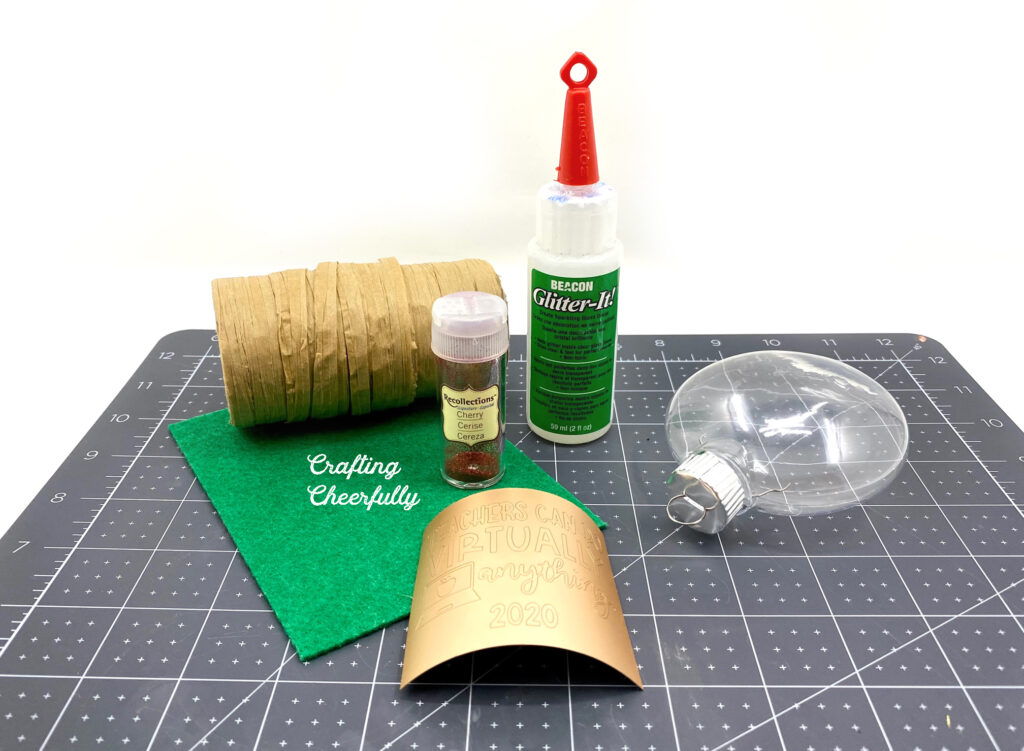 Supplies needed for glitter ornament craft sitting on a black self healing mat.