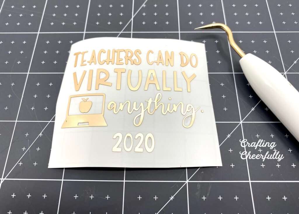 Adhesive foil cut in the words "Teachers can do virtually anything 2020" laying on a black self-healing cutting mat next to a weeding tool.