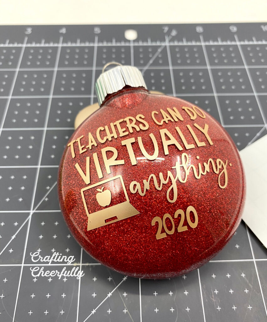 Red ornament with gold adhesive vinyl added to it with the message "Teachers can do virtually anything" and the date.