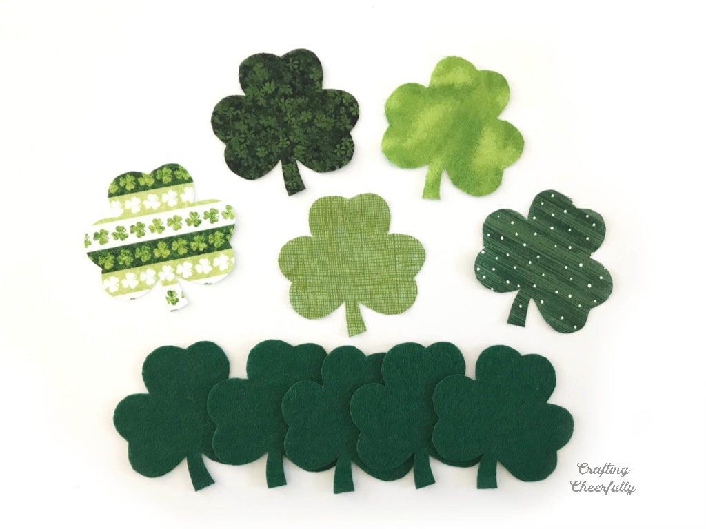 Five fabric shamrocks and five green felt shamrocks on a white background.