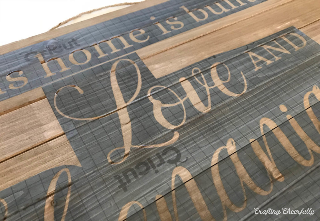 Stencils with the words "This home is built on love and shenanigans" is adhered to a wooden board.