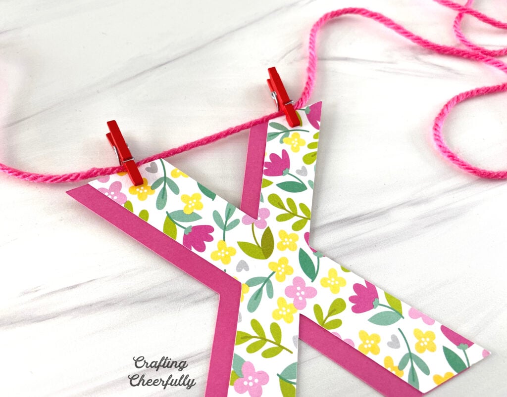 The paper X is attached to pink string using mini red clothespins.