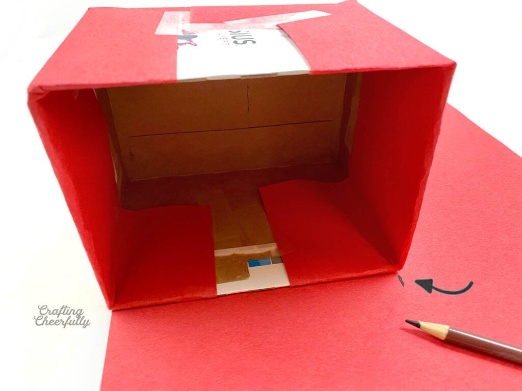 A brown pencil marks a piece of red paper the width of the box. 