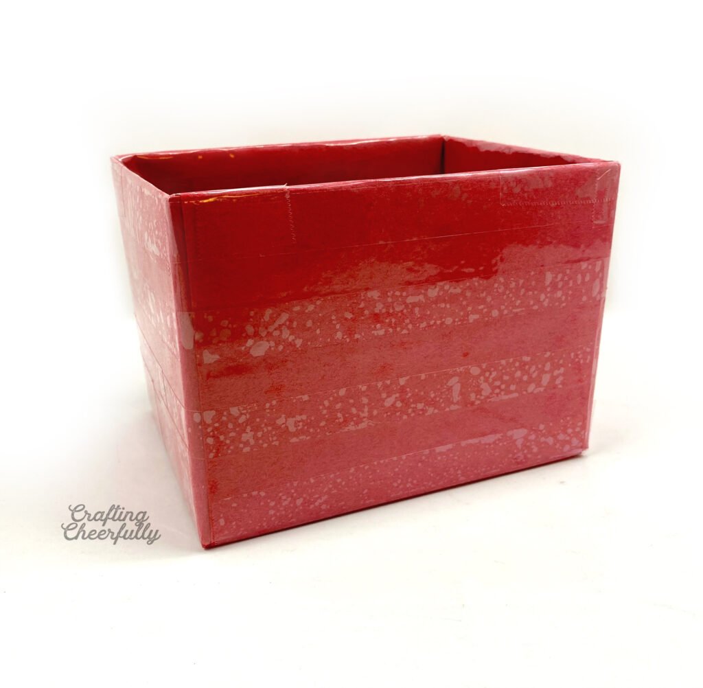 A box is covered in red construction paper and clear packing tape.