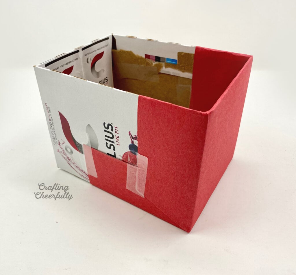 Red paper is taped to one end of the cardboard box.