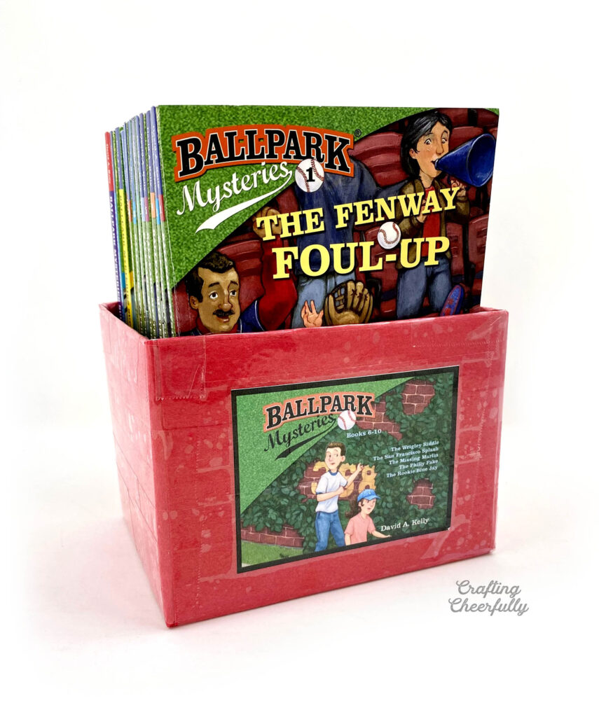 Red book bin filled with books from the "Ballpark Mysteries" series.