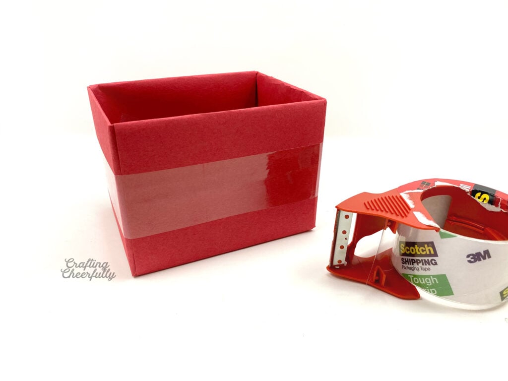 Clear packing tape is laying next to a red box.