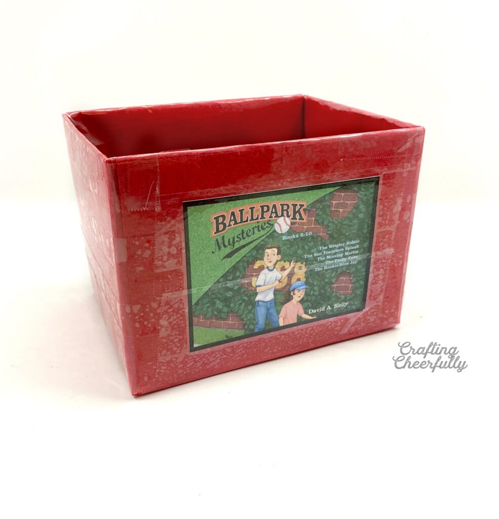 A box covered in red construction paper is sitting on a white table with a label for the books series on the front of it.