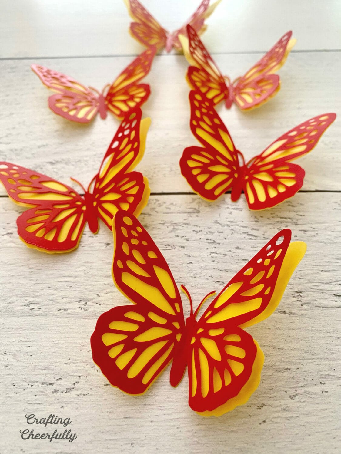 Red and yellow butterflies made from craft plastic are arranged on a wooden surface.