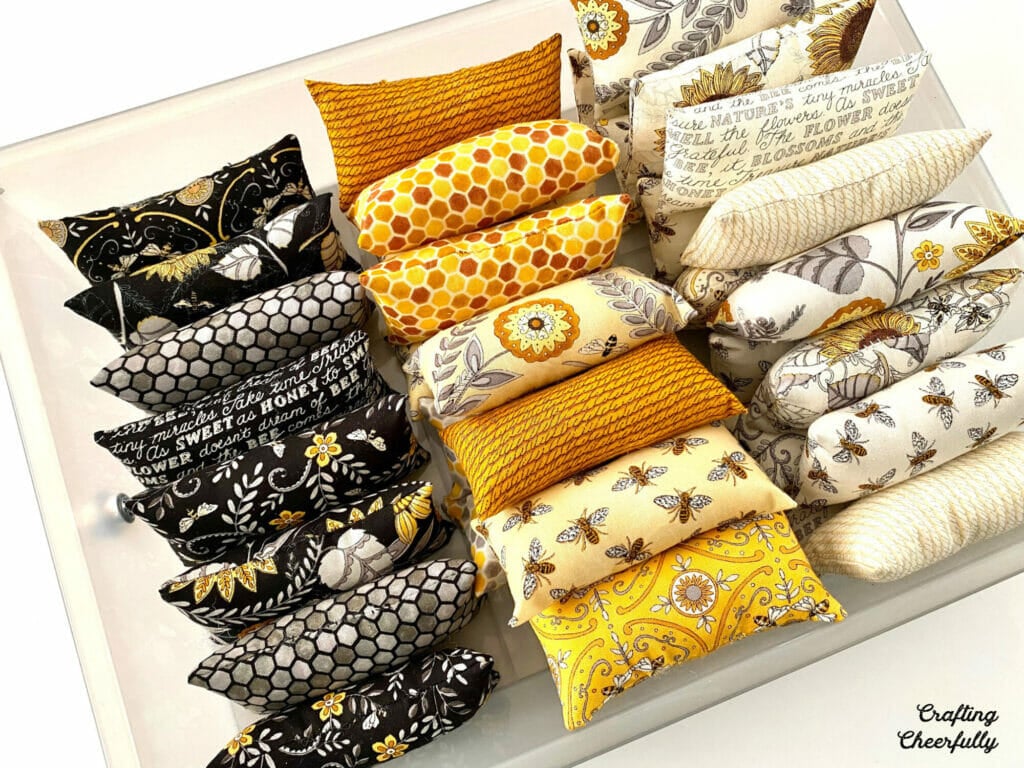 Mini fabric pillows in black, yellow, gray and white fabrics arranged in a plastic tray.