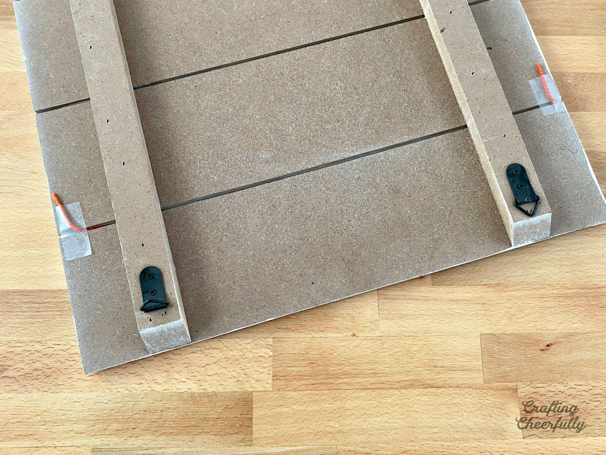 The back of the wooden board shows orange twine taped to it.