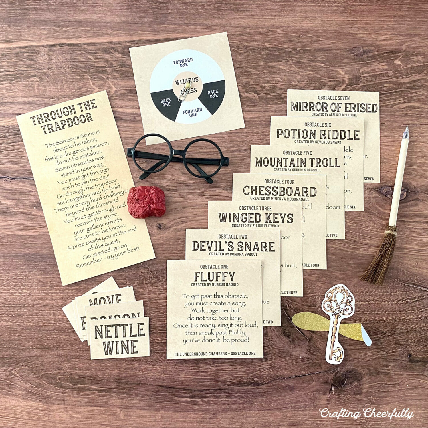 Harry Potter printable game cards lay on a table with a red sorcerer's stone, black glasses and a broom pen.