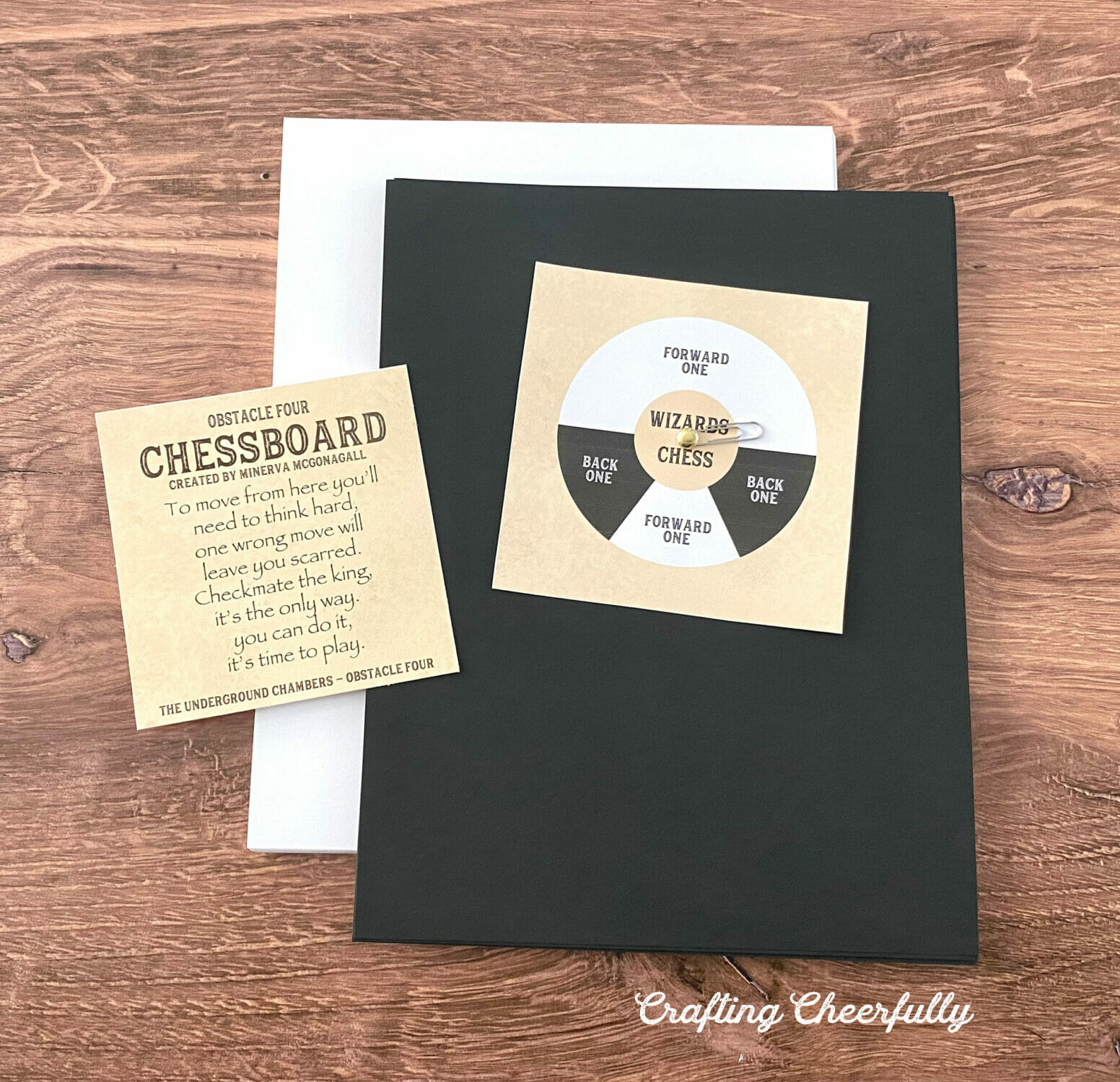 A stack of black paper and a stack of white paper sit on a table with a game card and printable spinner.