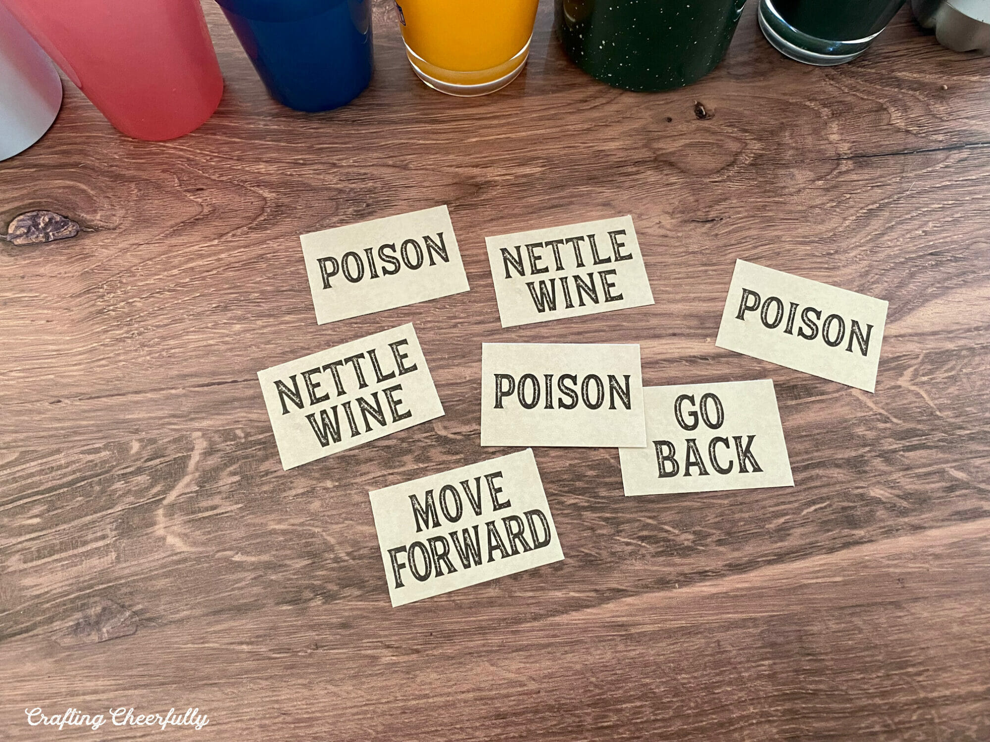 Small game cards that read Nettle Wine, Poison, Go Back and Move Forward lay on a table in front of cups.