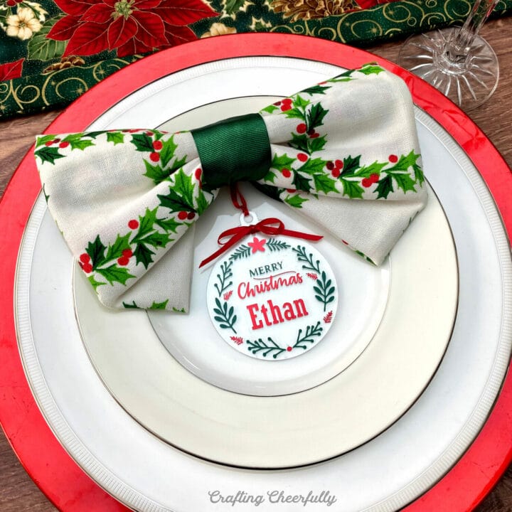 Christmas ornament place card holder lays on a plate at a holiday place setting.