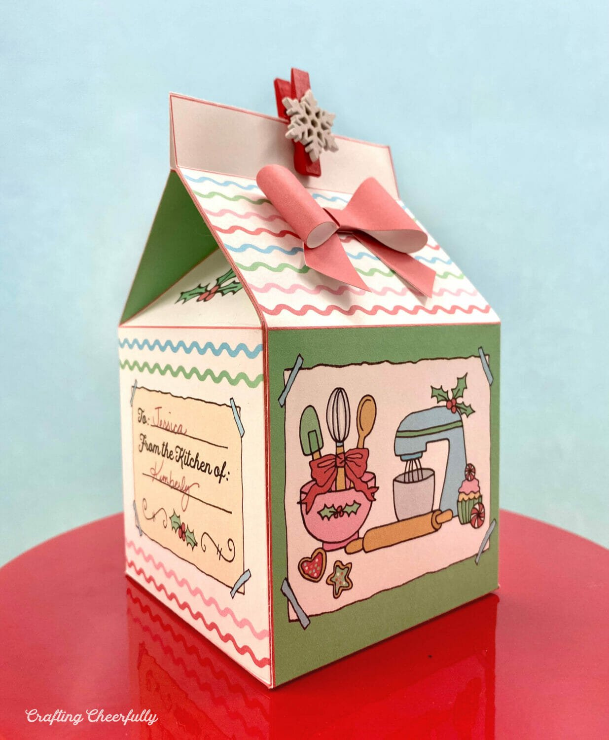 A Christmas cookie treat box sits on a red cake stand.