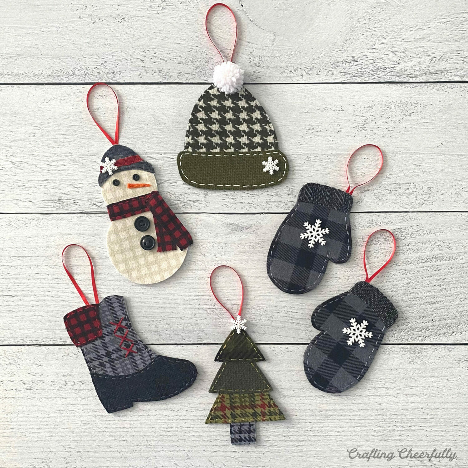 Fabric ornaments including winter hats, mittens, tree and boot lay on a white wooden table.