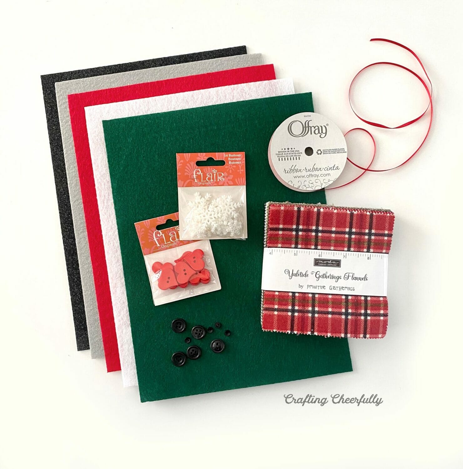 A stack of felt sits next to a charm pack, ribbon and buttons.
