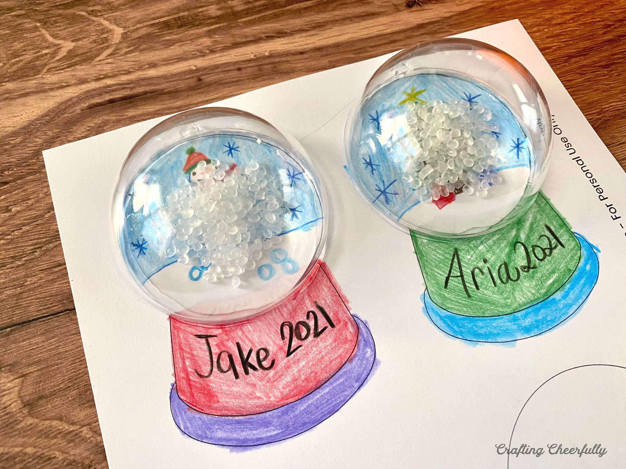 The snow globe template lays on a wooden table with plastic ornaments glued to the top of it. 