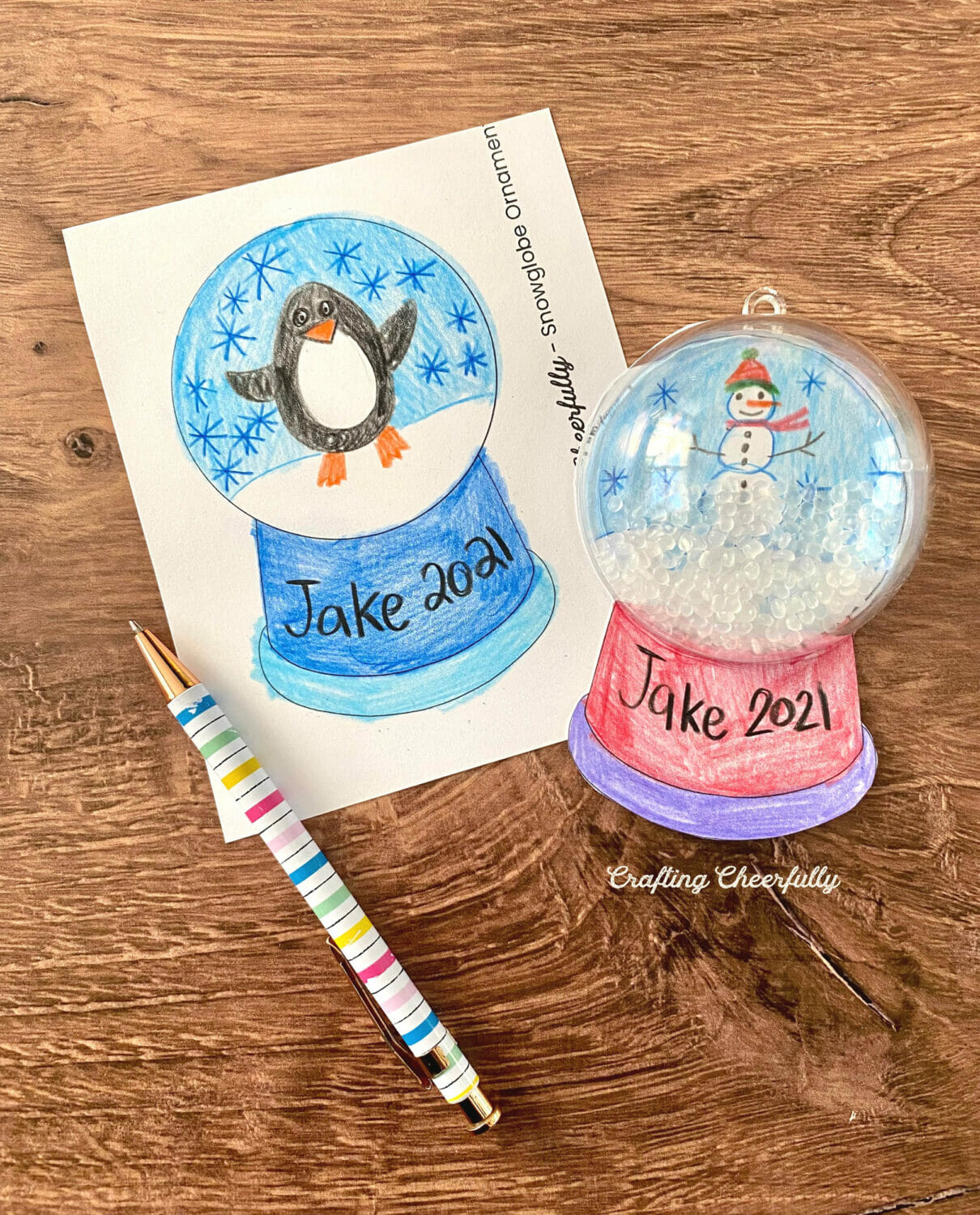 A partially finished snow globe ornament lays on a wooden table next to a template colored in.