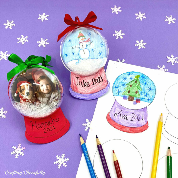 Two snow globe ornaments lay next to a snow globe coloring page on a purple surface with snowflake confetti around them.