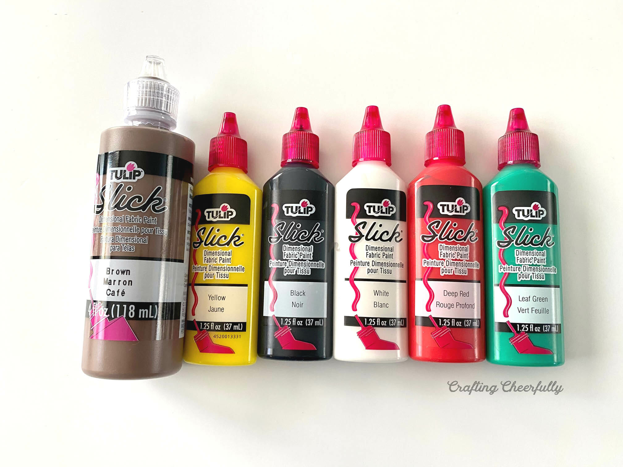 Bottles of dimensional fabric paint are lined up on a white table.
