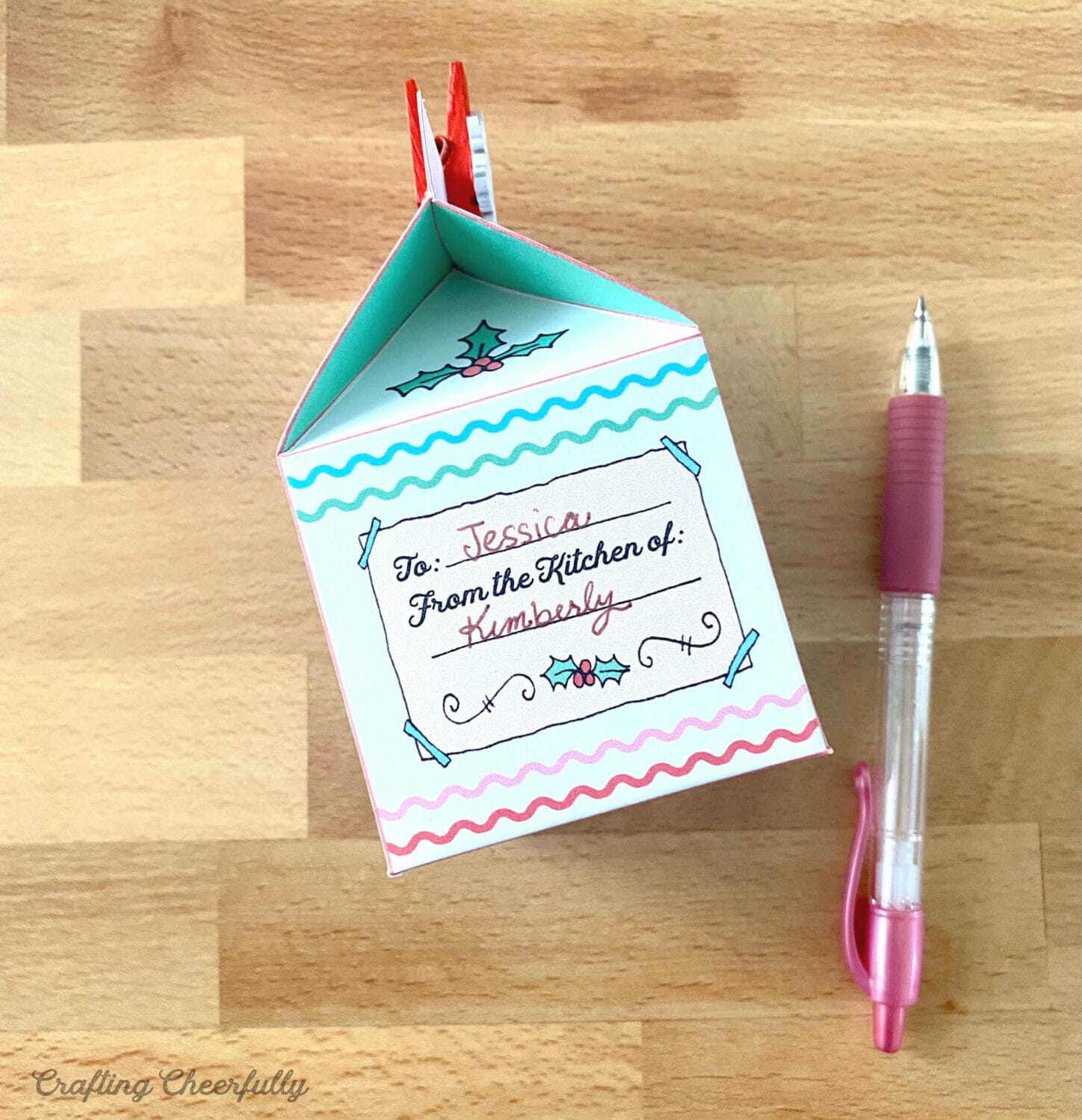A paper treat box lays on a table next to a pink pen.