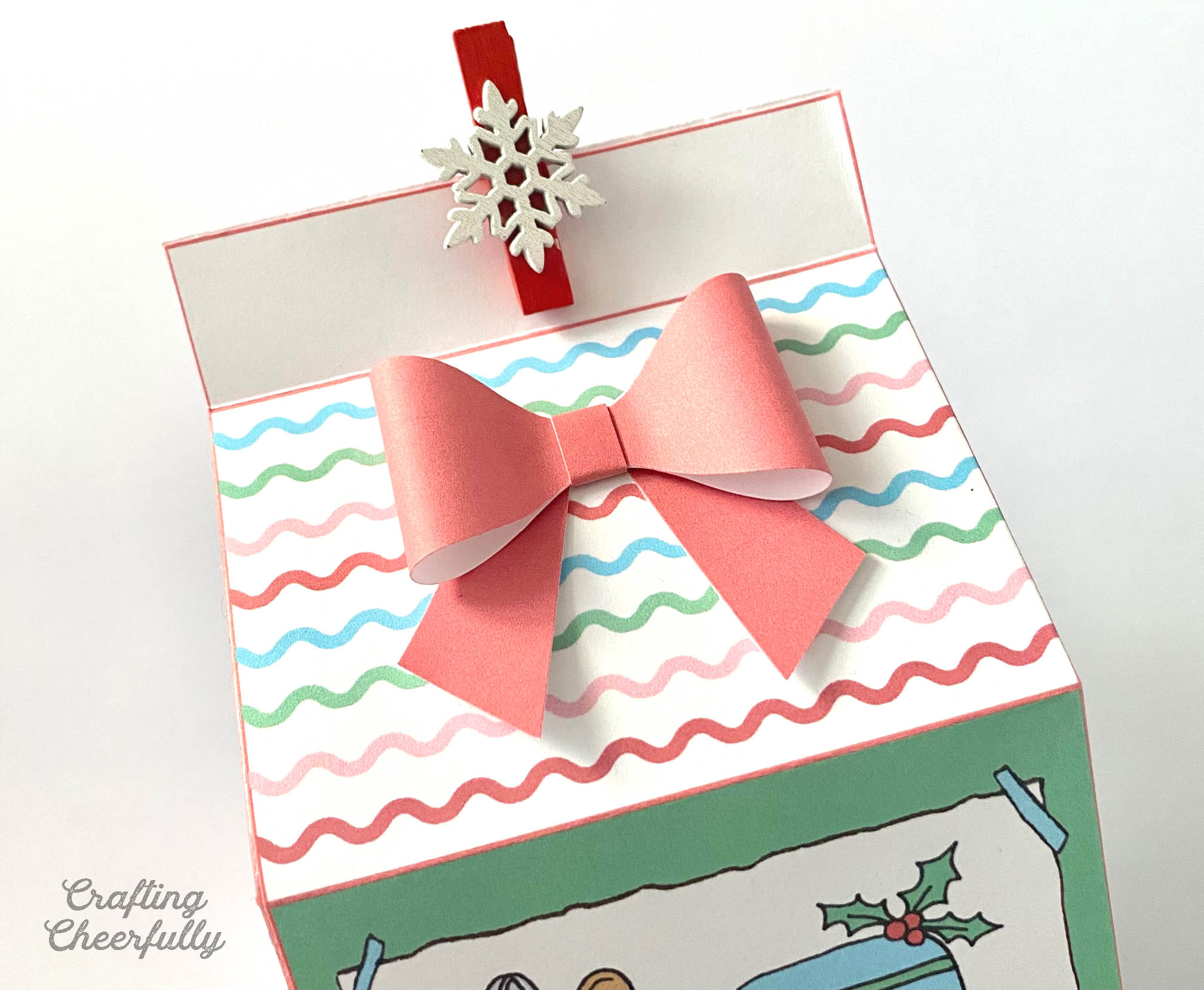 A pink bow on top of a printable treat box with a red and white snowflake clothespin at the top.