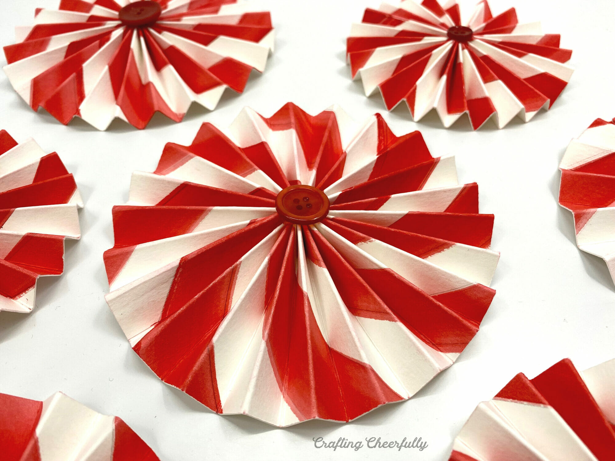 Peppermint paper rosettes lay on a white table with red buttons in the center of each.