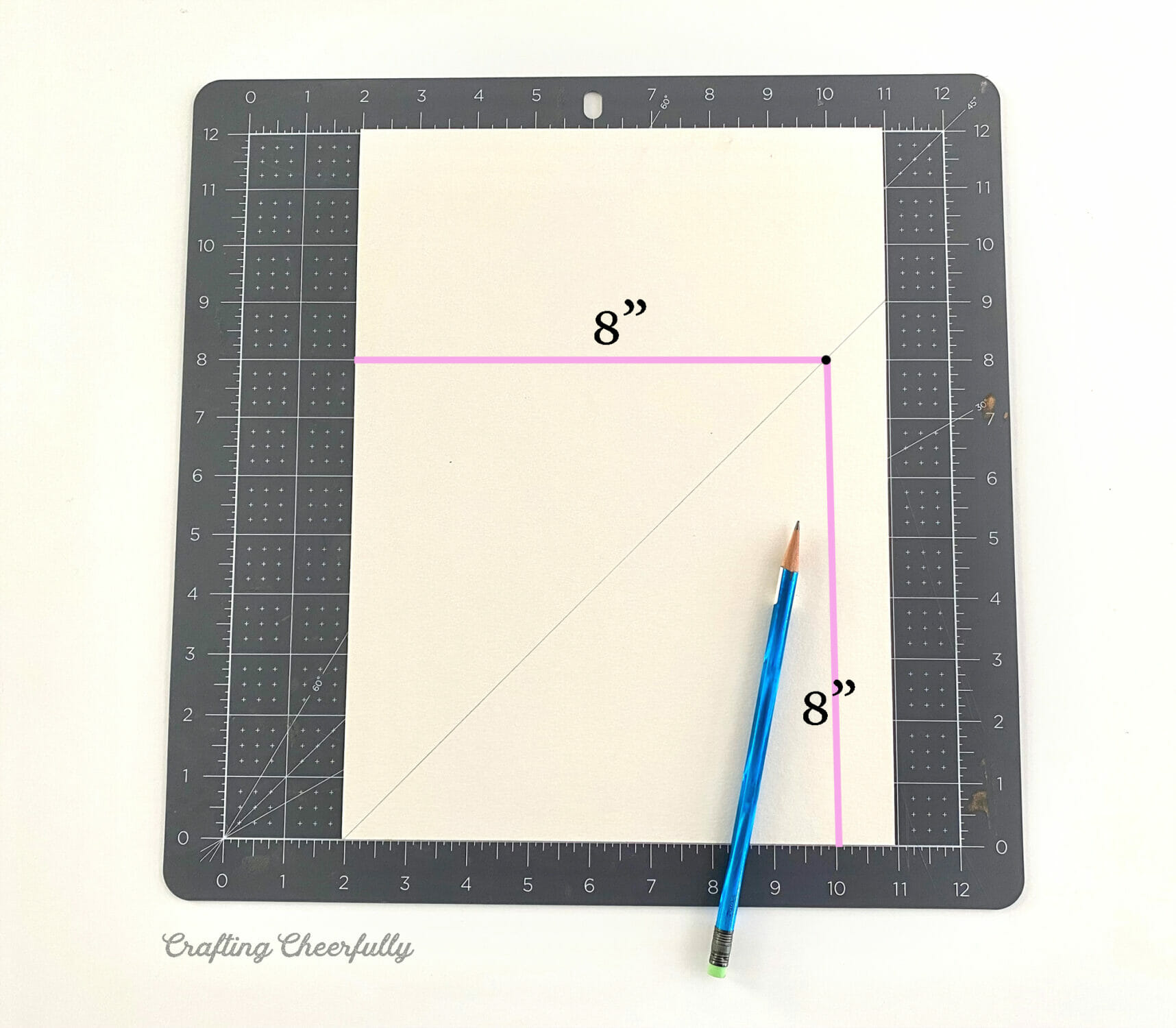A piece of white watercolor paper lays on a black cutting mat. Diagonal lines are drawn on it with pencil using an 8" guide.