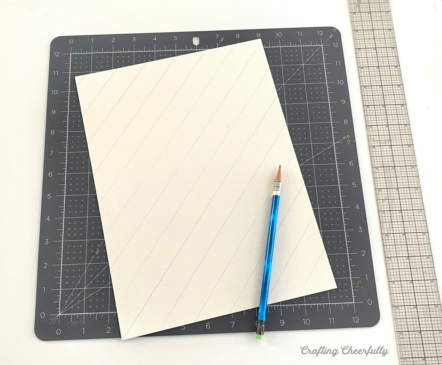 Diagonal lines are drawn with pencil across a piece of white watercolor paper with a pencil.