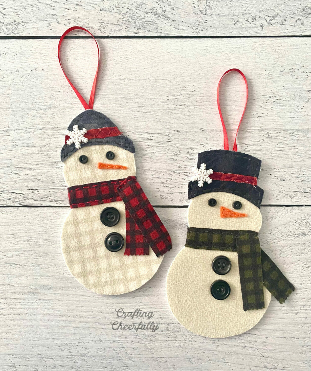 Two fabric snowmen ornaments in scarves and hats lay on a white wooden table.