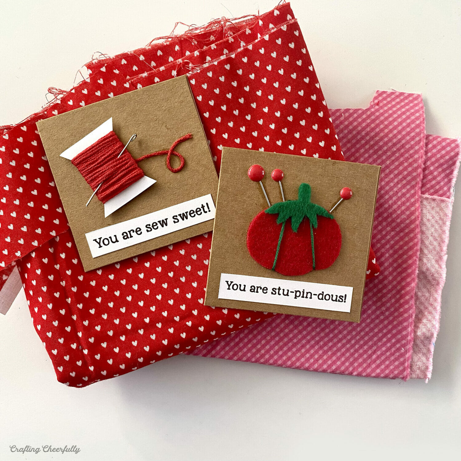 Sewing-themed valentines lay on a stack of red and pink fabric.