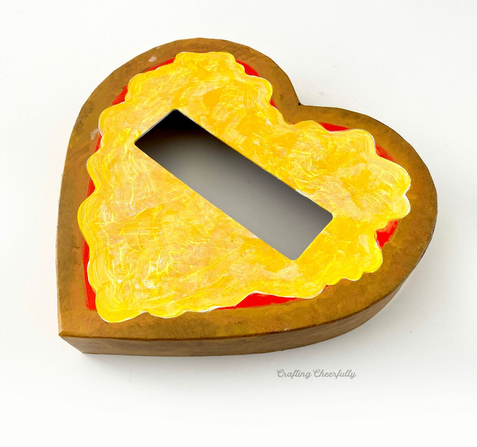 A layer of yellow paint covers the white paint of the cheese on the heart shaped pizza box.