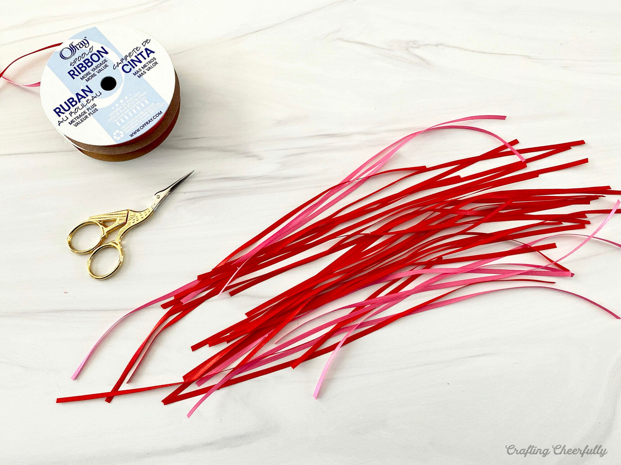 Strips of red and pink ribbon lay next to a scissors and roll of ribbon.