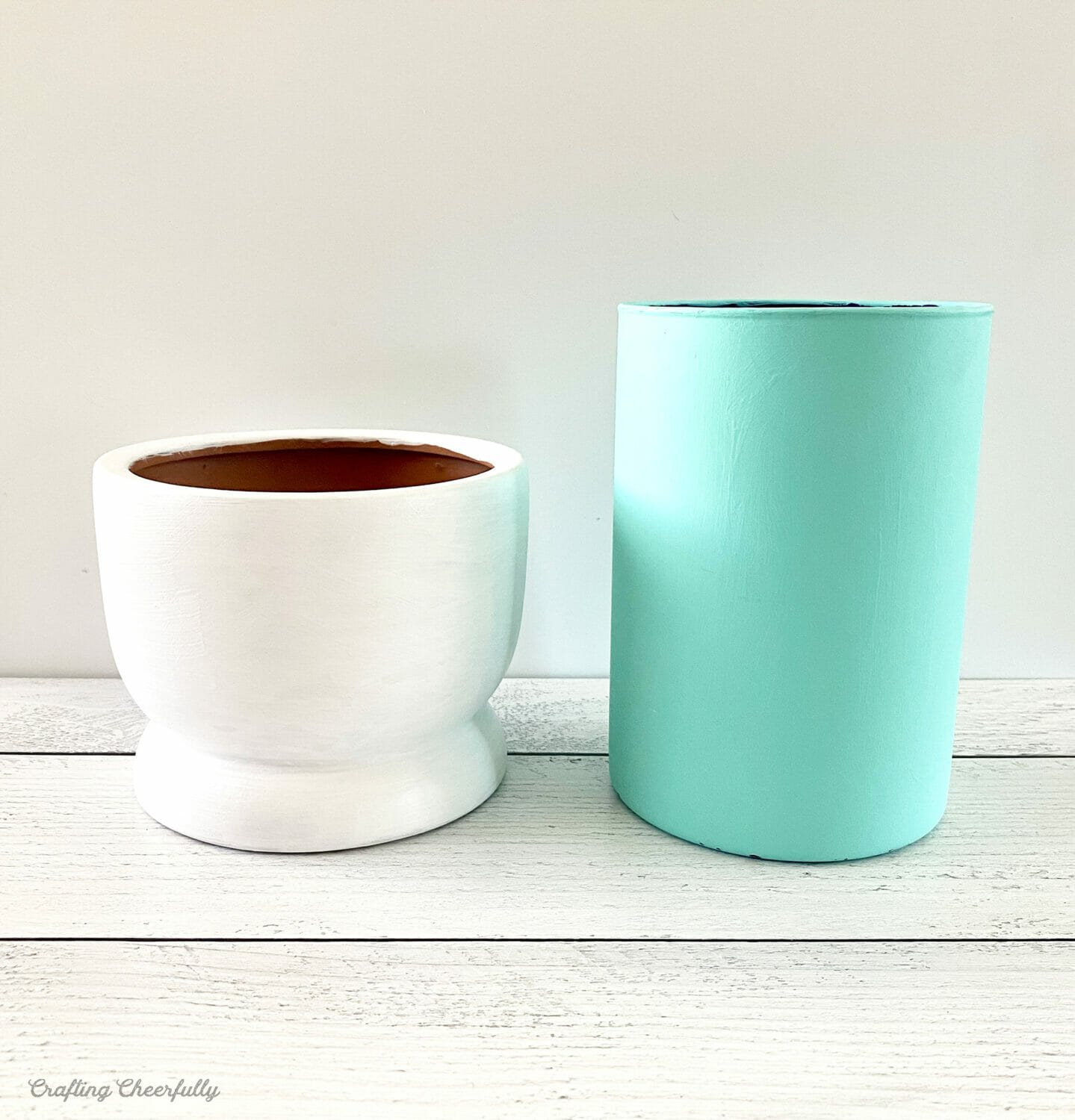 A short white vase sits next to a teal teal vase.