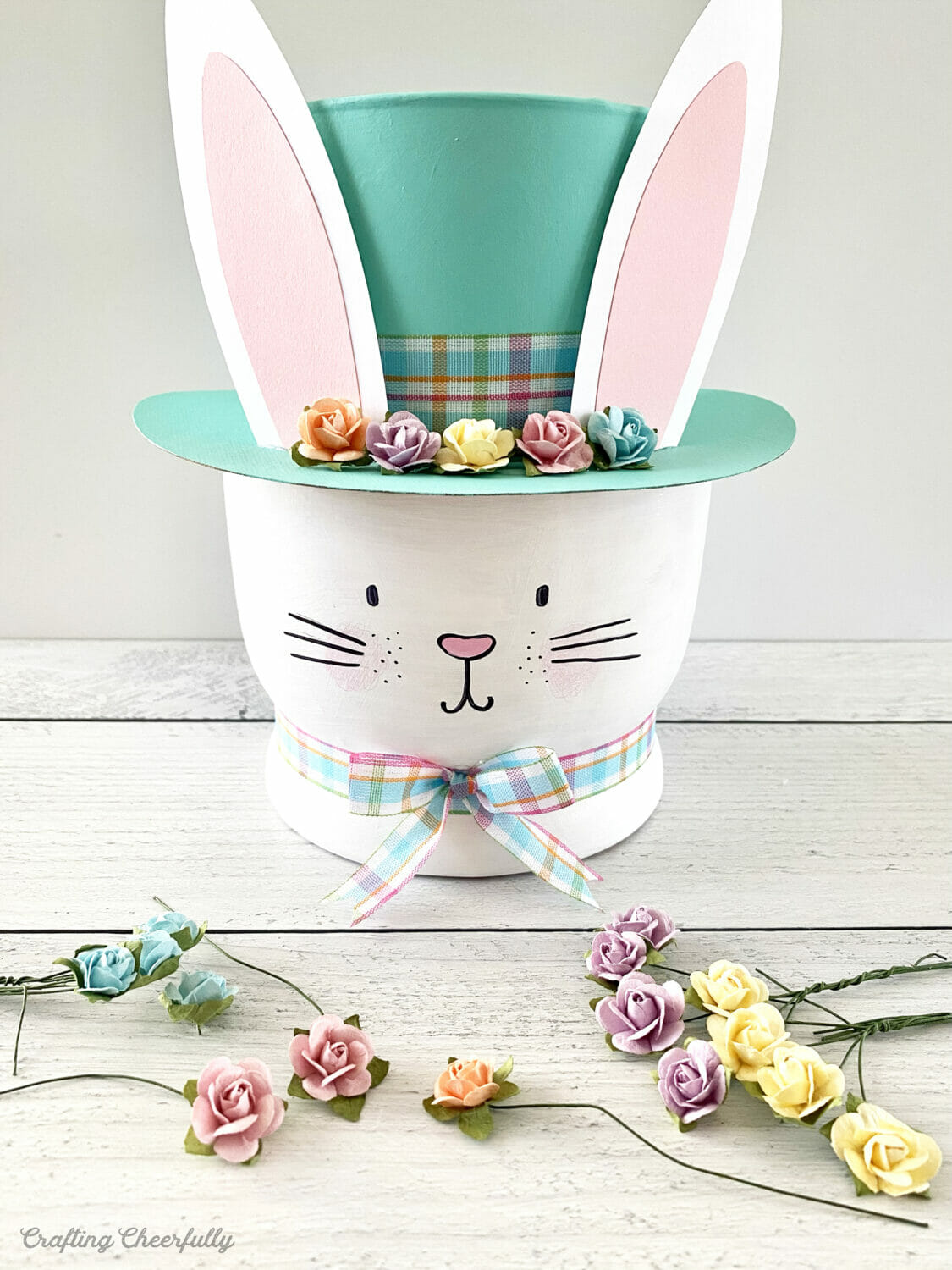 Tiny craft flowers in pastel colors lay in front of the bunny vase.