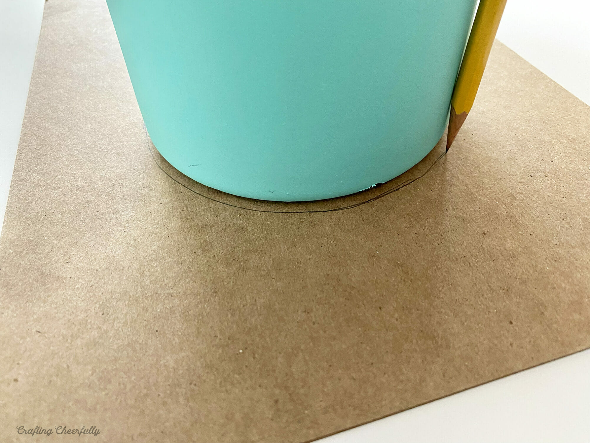 A pencil tracing around the bottom of a teal vase onto chipboard.