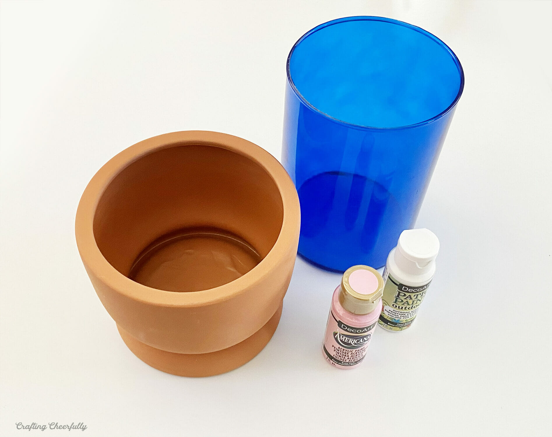 A short terra cotta vase, a tall blue glass vase and two bottles of paint.