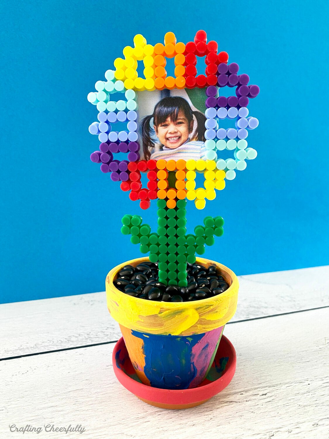 A painted flower pot with a perler bead flower frame in it.