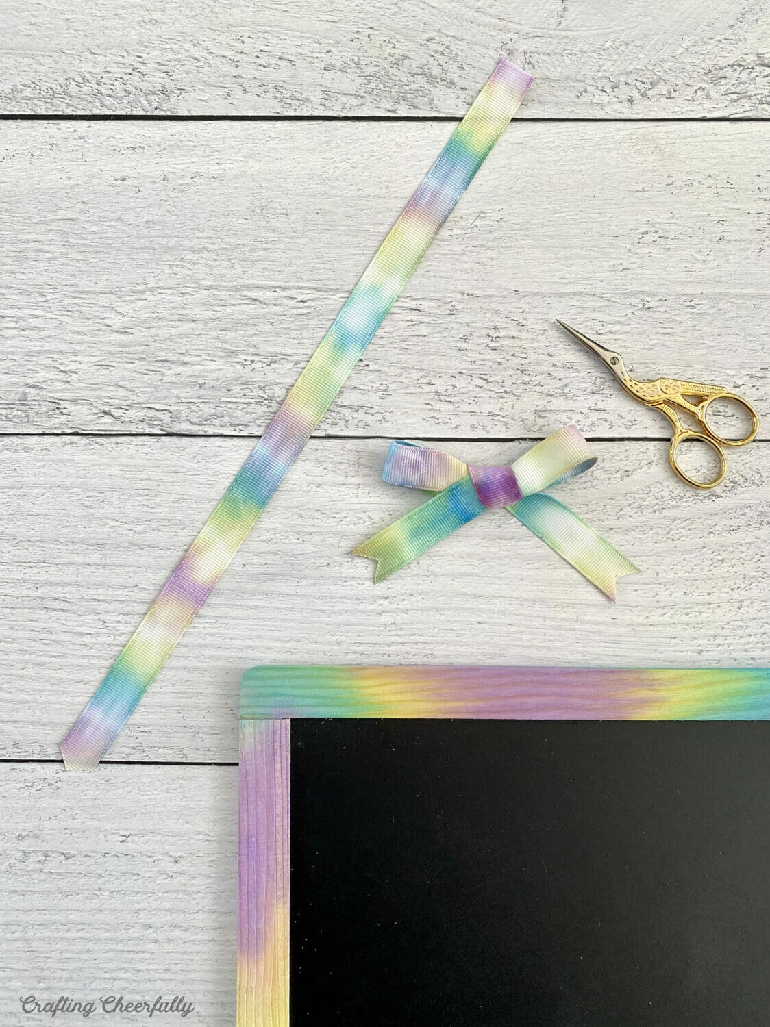 Tie dye ribbon is made into a handle and a bow, ready to be applied to the chalkboard.