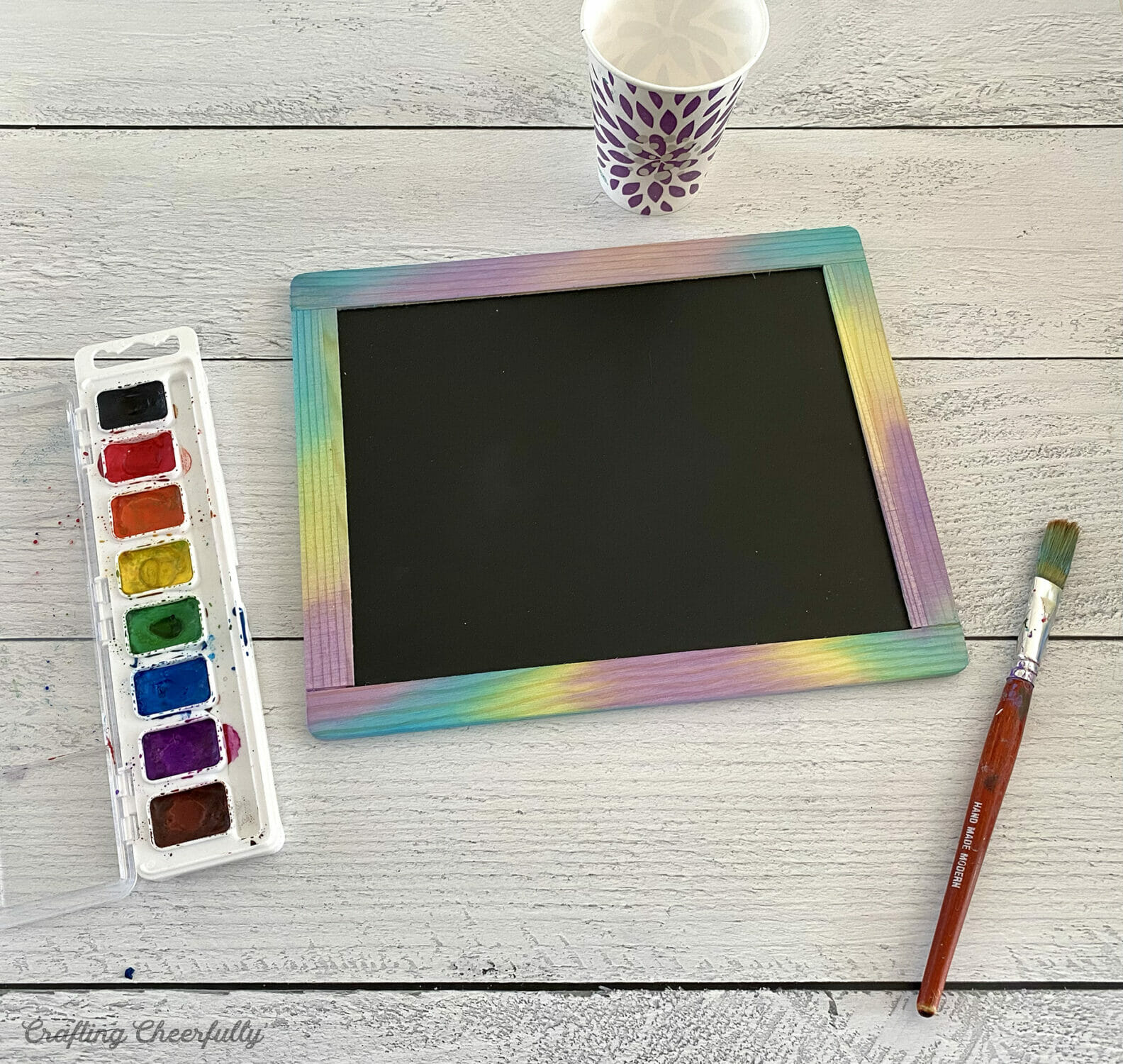 A wooden framed chalkboard is painted with watercolor paint.