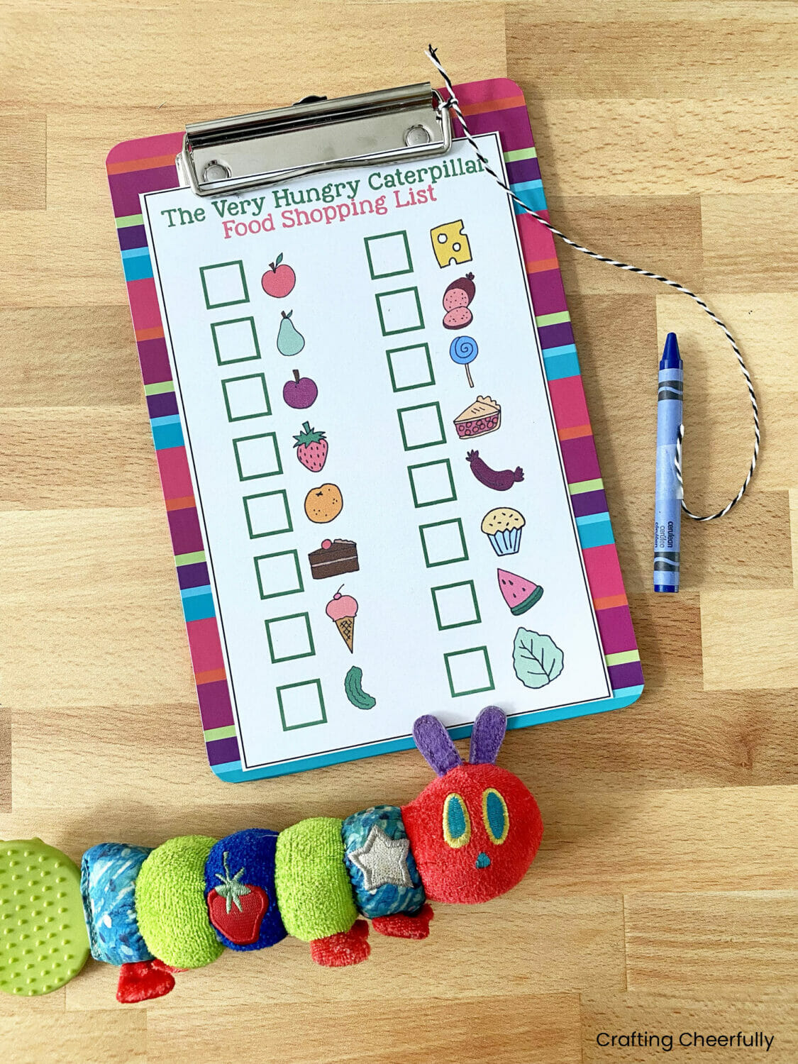 Printable shopping list on a mini clipboard next to a Hungry Caterpillar toy.