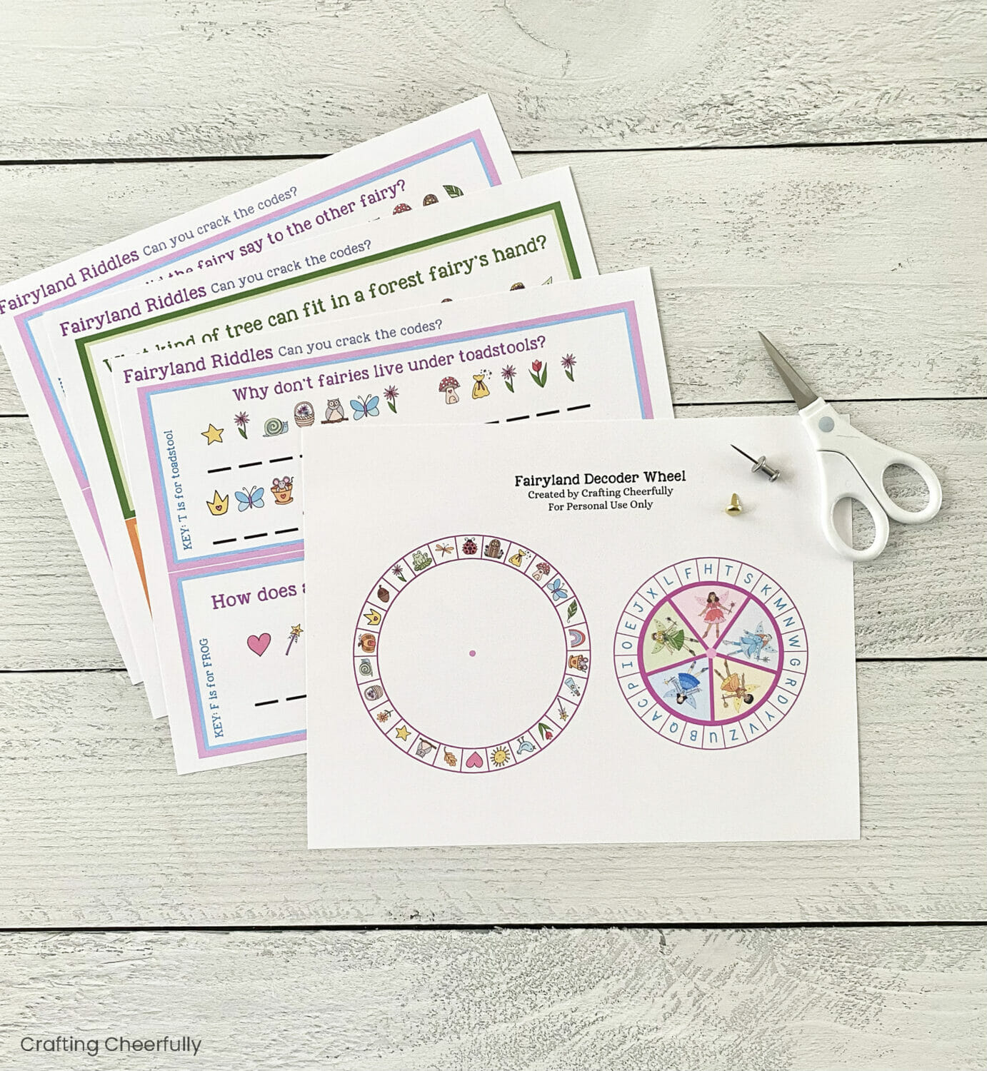 Printable worksheets with the fairy decoder wheel and riddles lay next to scissors.